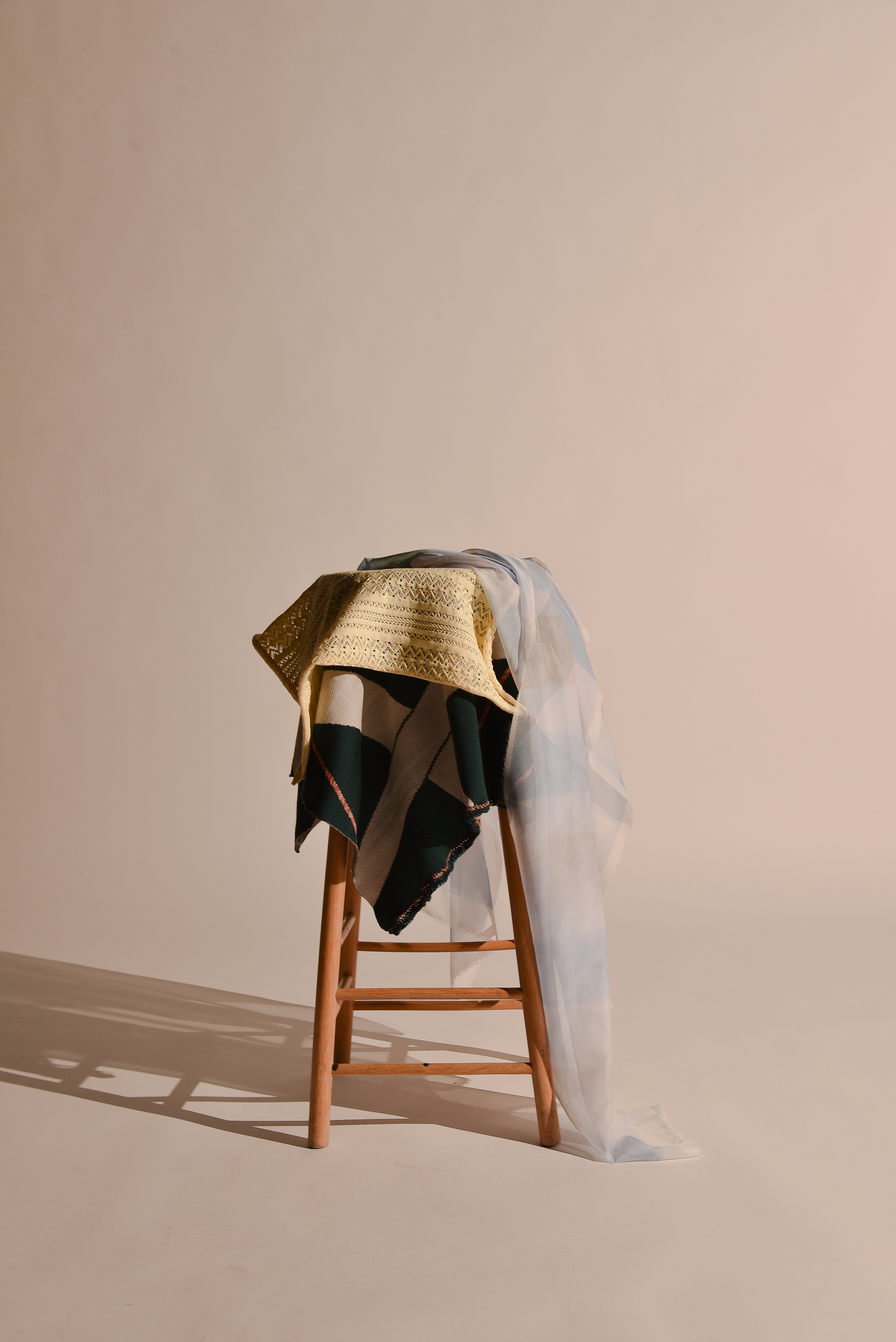 Knitted and printed fabrics draped on a wooden stool 